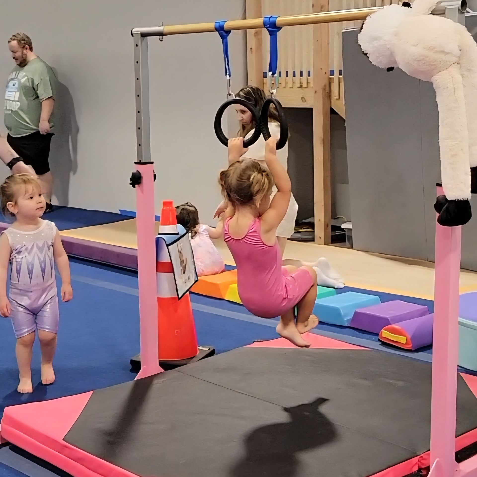 Smiling baby wearing a helmet and bow on a balance beam, indoors.