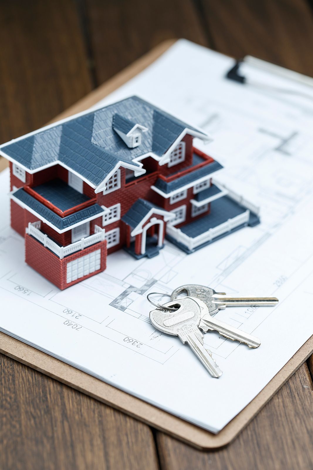 Maqueta de casa, llaves y portapapeles sobre superficie de madera, posiblemente para uso inmobiliario.