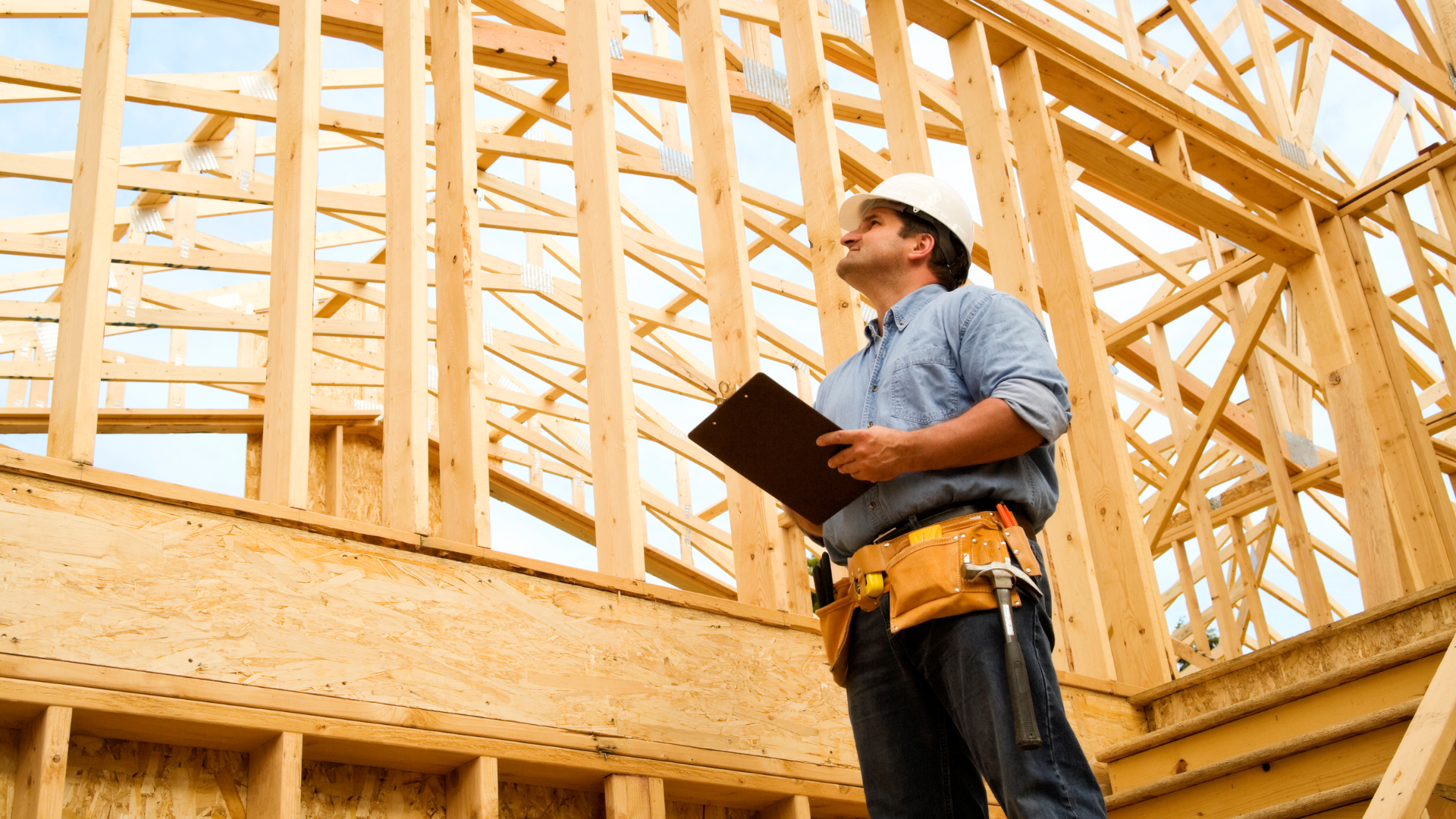 Construction worker holding a clipboard inside a wooden house frame under construction