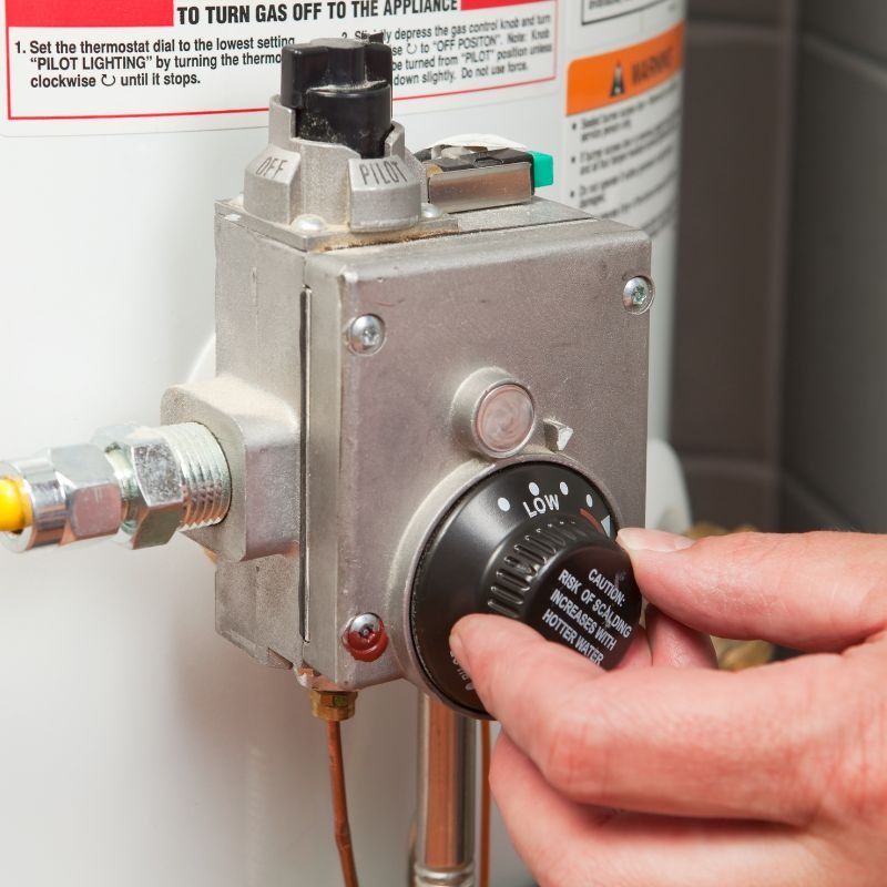 Person turning a black knob on a gas appliance control box