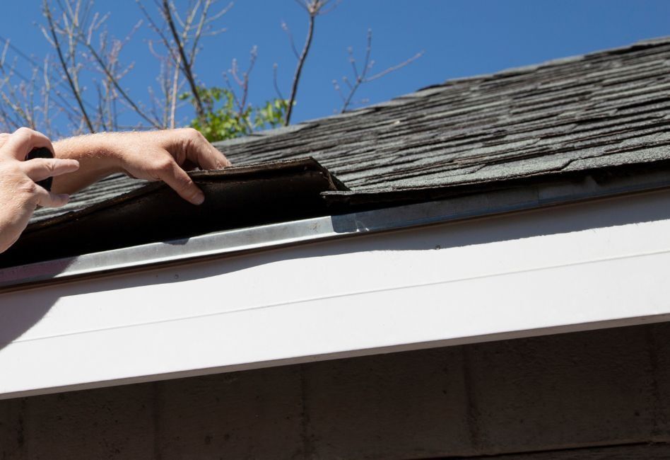 Hand placing a shingle on a roof edge under a blue sky