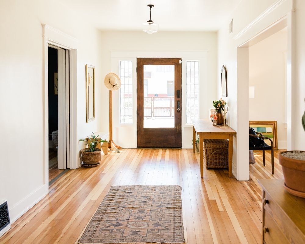 Bright hallway with hardwood floors, a rug, console table, mirror, and front door with sidelights.