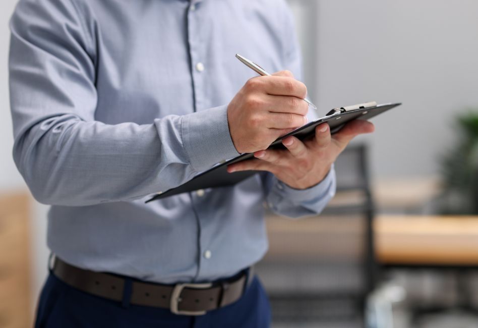 Person in a light blue shirt writing on a clipboard in an office setting