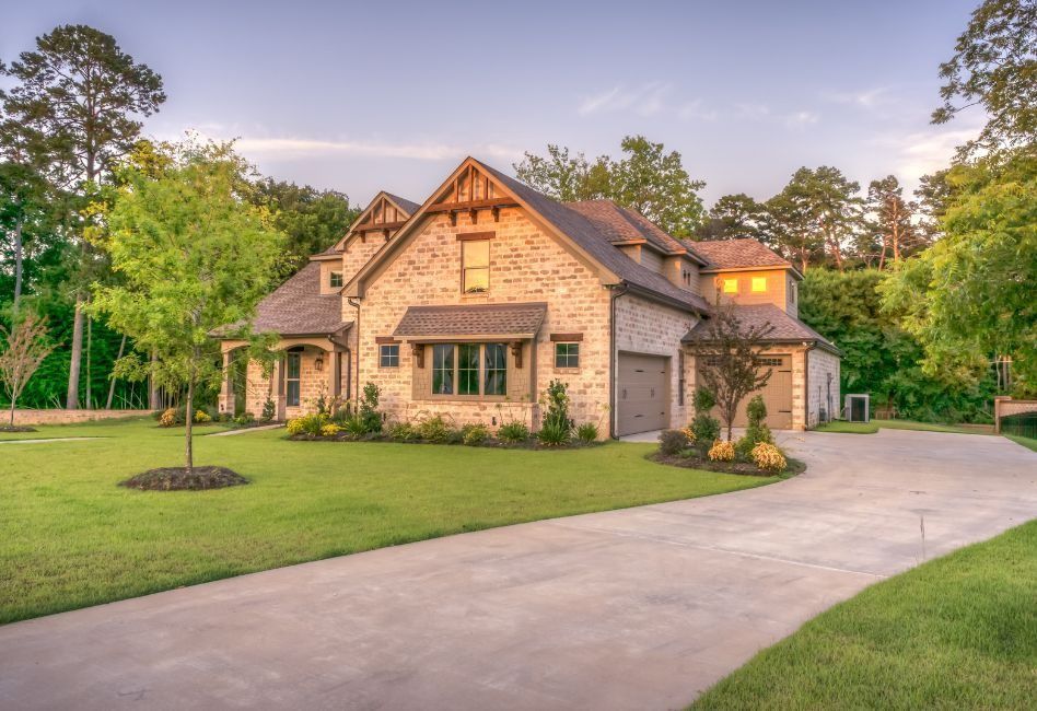Large stone house with a manicured lawn and curved driveway at sunset