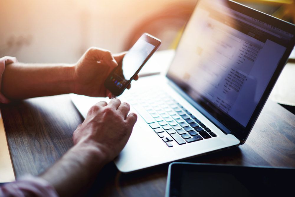 A person is typing on a laptop while holding a cell phone — New Hire in Newcastle, NSW