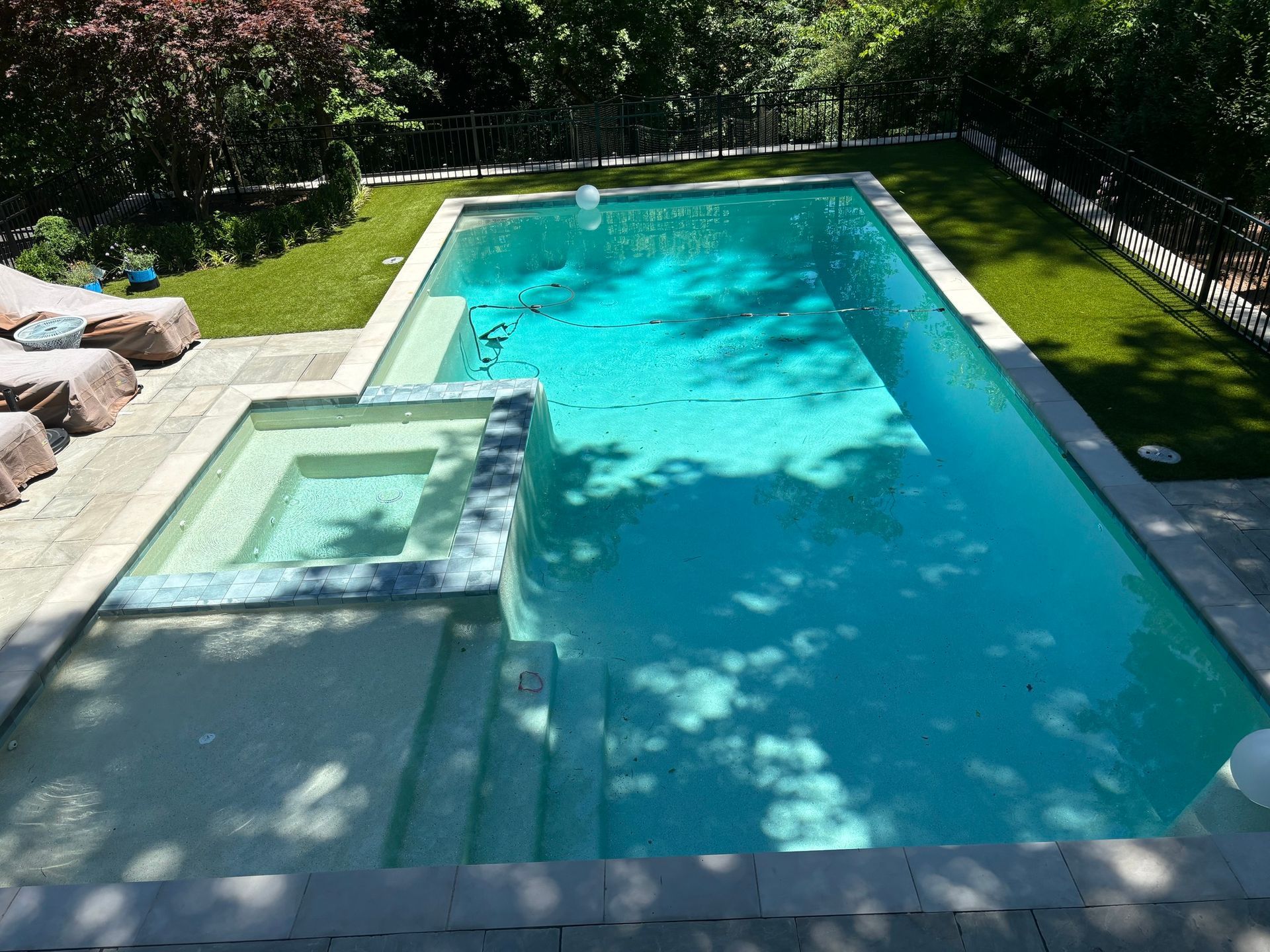 Swimming pool and spa in a backyard with light blue water, surrounded by grass and stone.