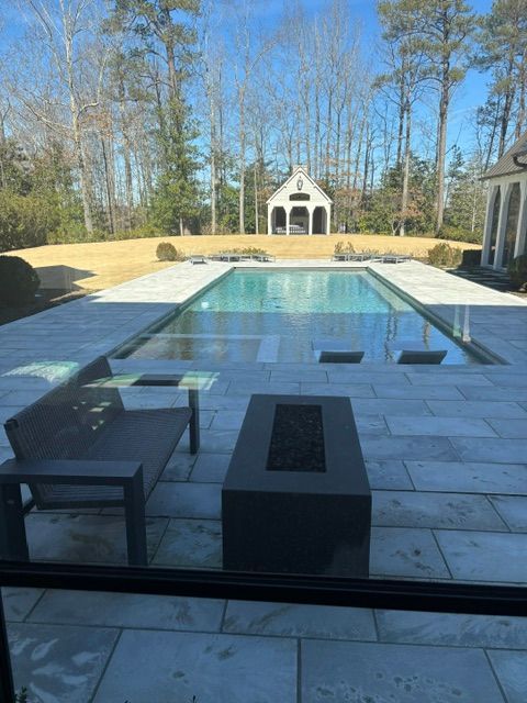 Backyard with a pool, patio, and fire pit, with a small structure in the background.