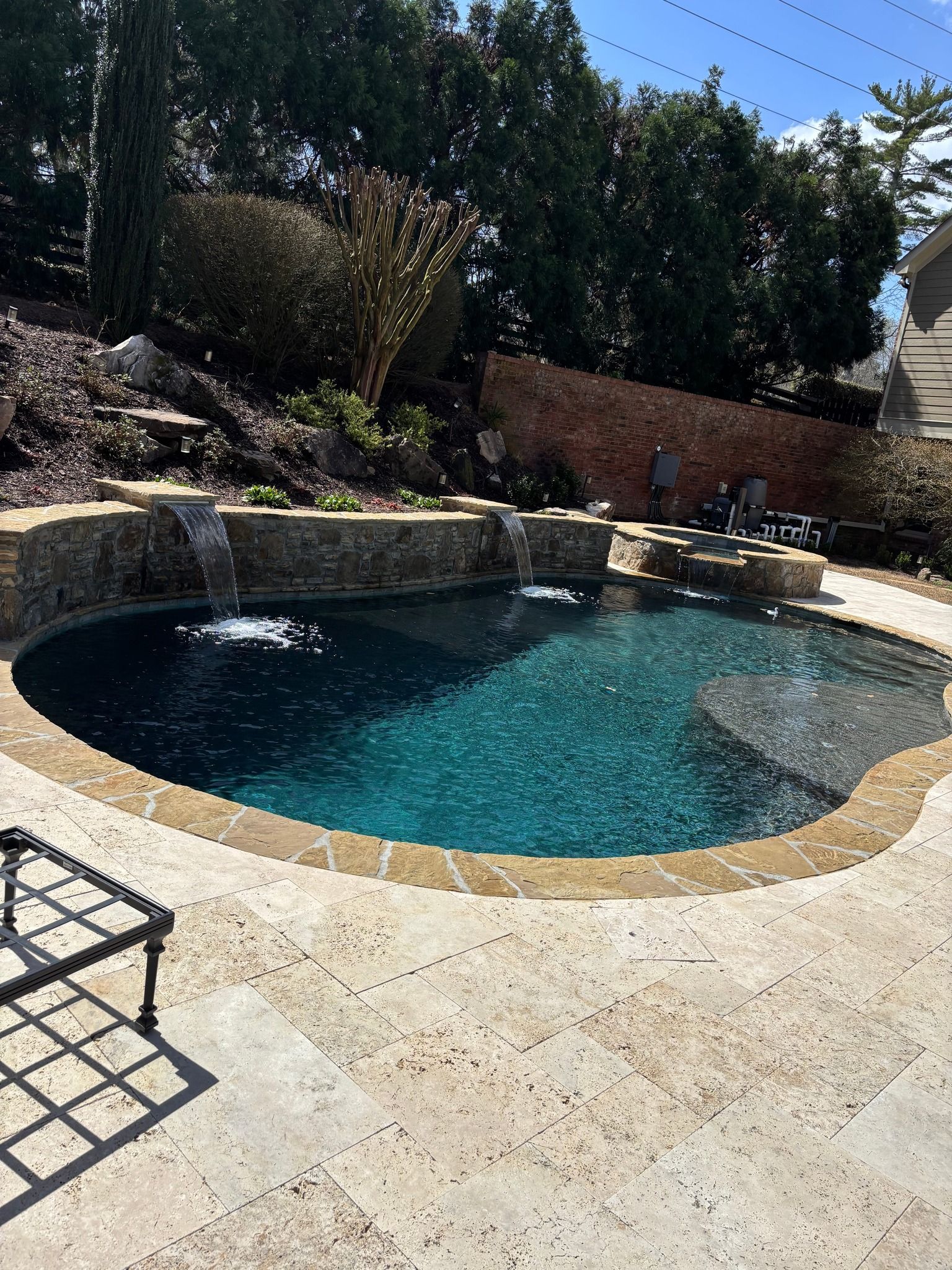 Swimming pool with a waterfall feature surrounded by stone and landscaping.
