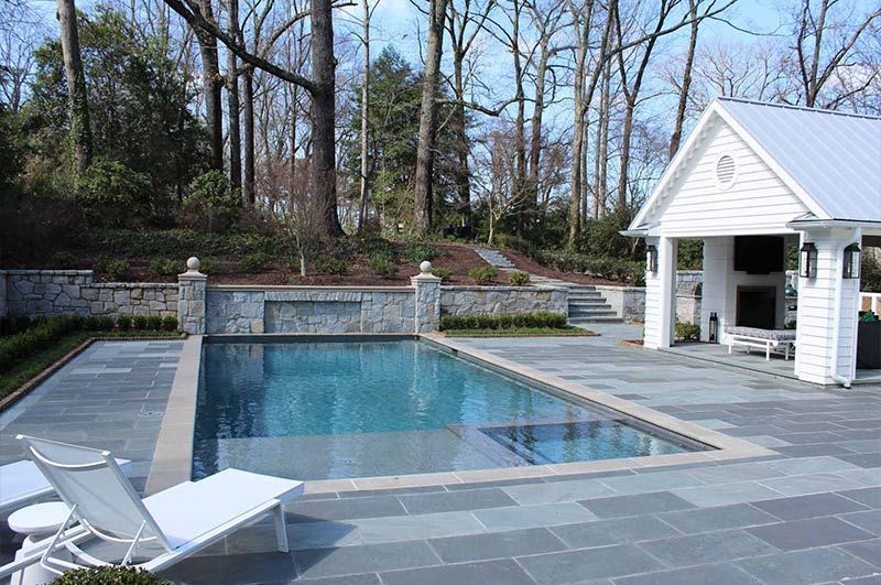 Poolside scene with pool, white gazebo, and lush greenery.