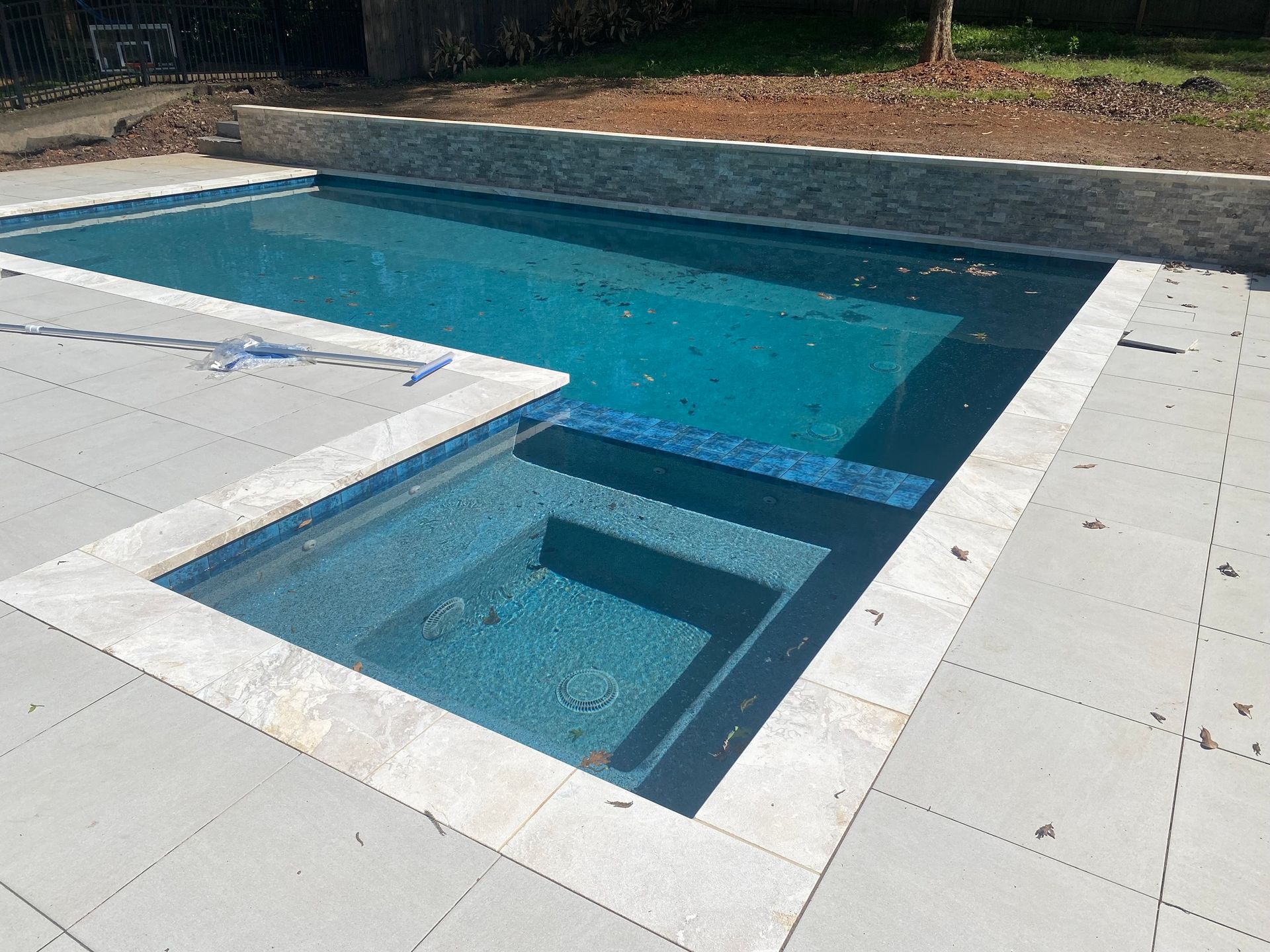A partially constructed pool with blue water, gray tiling, and a stone border.