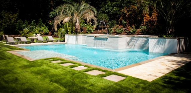 Luxurious outdoor pool with waterfall and lounge chairs surrounded by lush greenery.