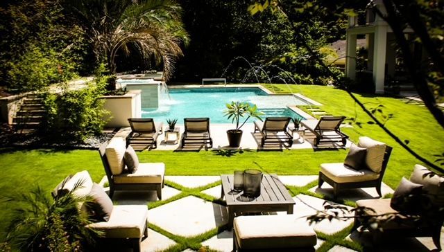 Lush backyard with pool, lounge chairs, seating area, and verdant landscaping.