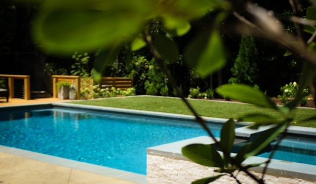 Pool with turquoise water surrounded by a lawn, trees, and a deck.