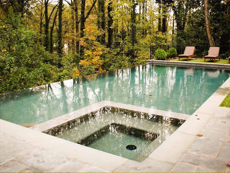 Swimming pool with built-in spa, surrounded by trees and lounge chairs in a natural setting.