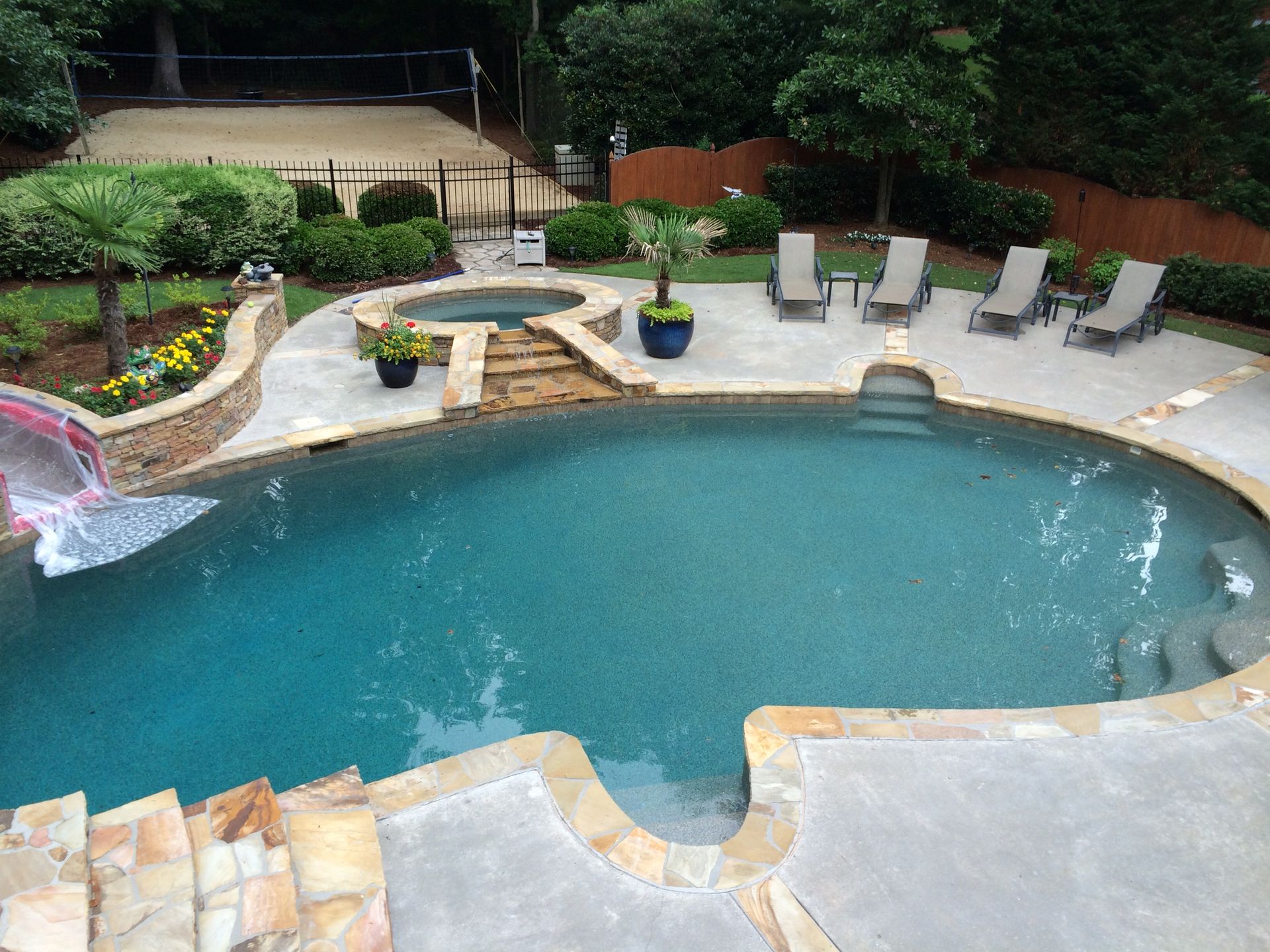 Swimming pool with waterfall, hot tub, lounge chairs, and lush landscaping.