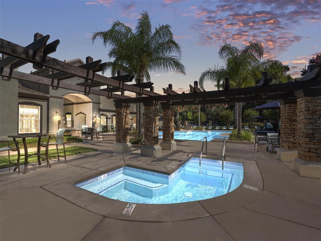 Outdoor pool area with a hot tub, palm trees, and lounge seating at an apartment community at River Oaks.