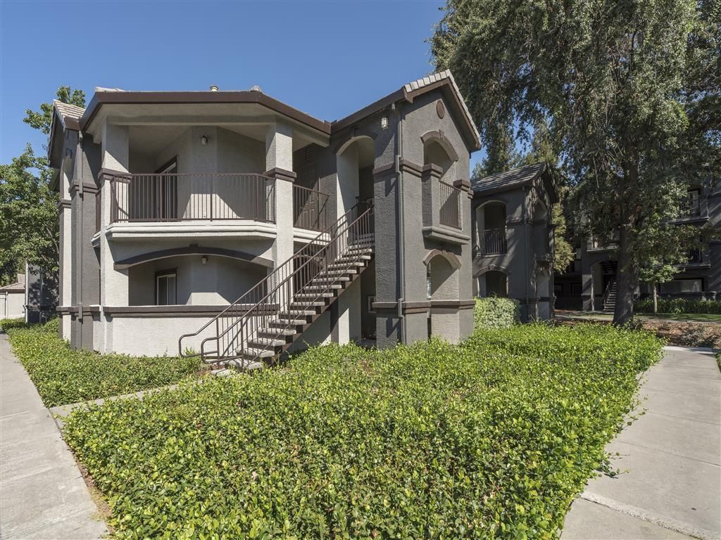 Exterior view of a gray multi-family building with stairs and landscaped hedges at River Oaks.