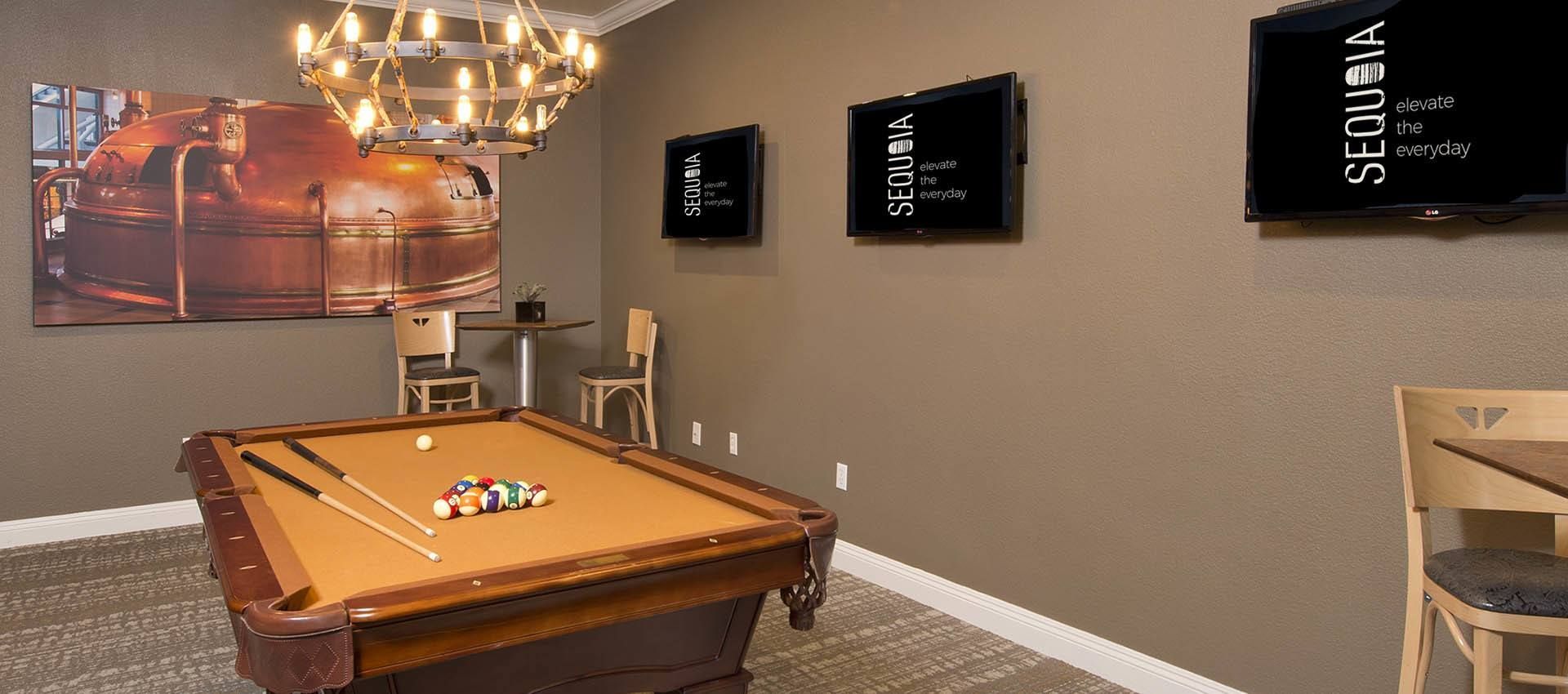 A game room with a pool table, wall-mounted TVs, and a large metal brewing tank art piece at River Oaks.