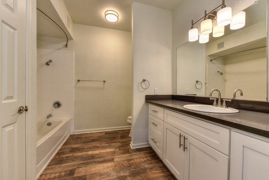 Bathroom with a long white vanity, dark countertop, large mirror, and tub/shower at River Oaks.