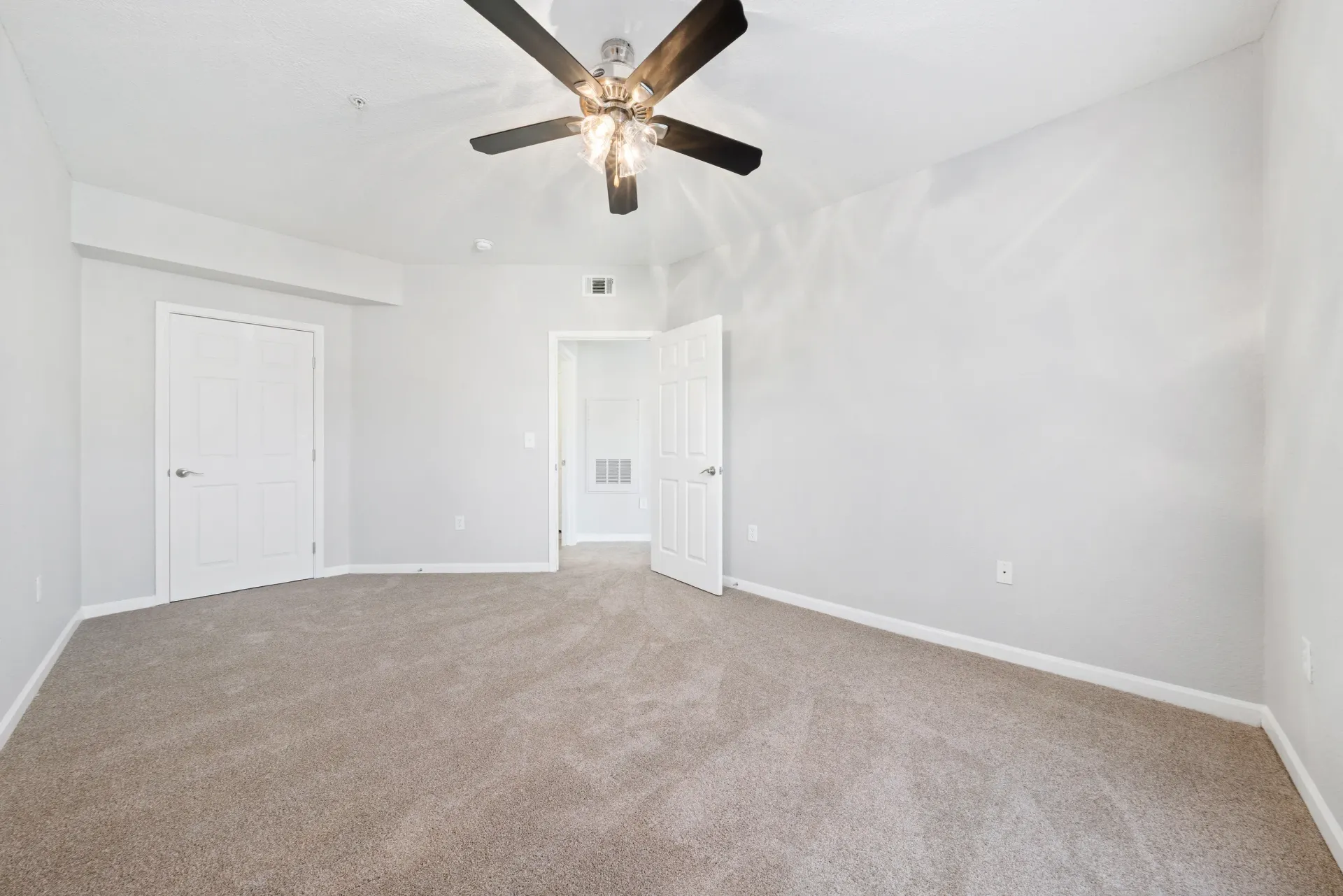 Empty bedroom with gray walls, tan carpet, two white doors, and a ceiling fan at River Oaks.