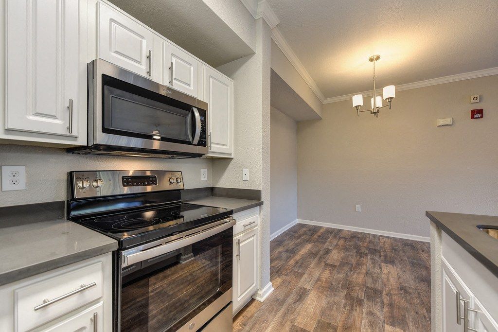 Kitchen in an apartment with white cabinets, stainless steel microwave and stove, and wood-look flooring at River Oaks.