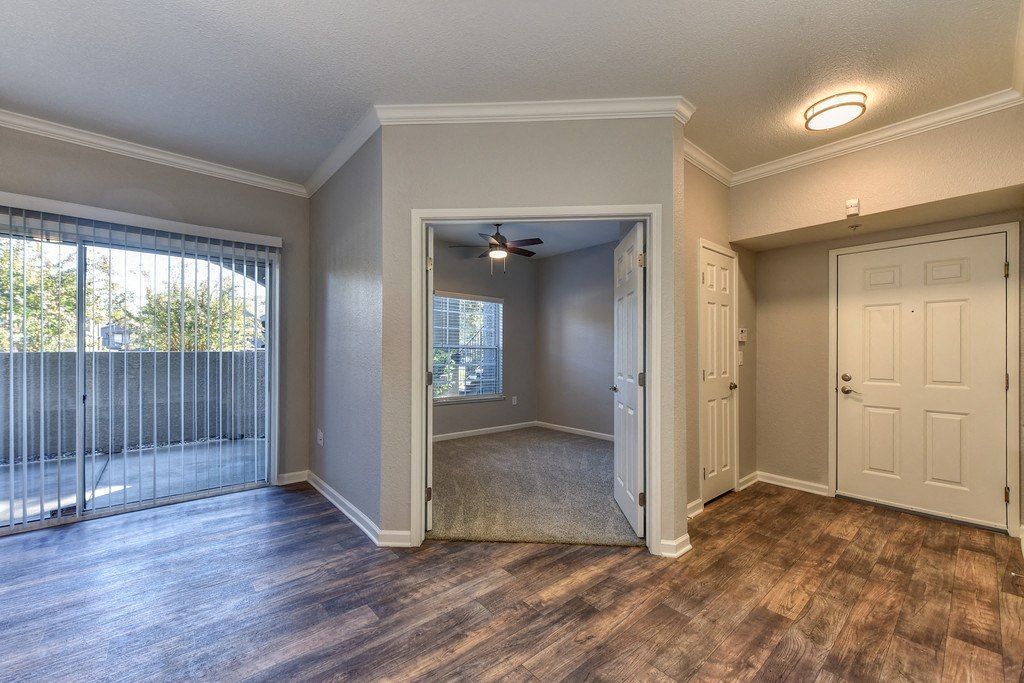 Living area with laminate flooring, sliding door to balcony, and a carpeted room near the entry at River Oaks.