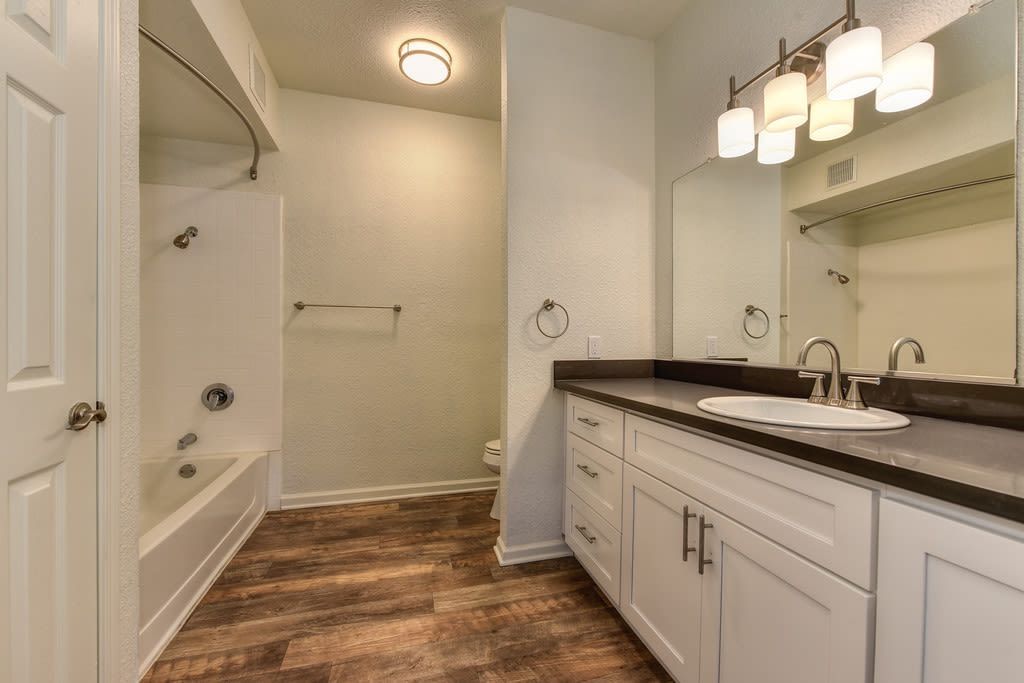 Bathroom with white cabinetry, brown countertop, brown flooring, tub/shower combo at River Oaks.