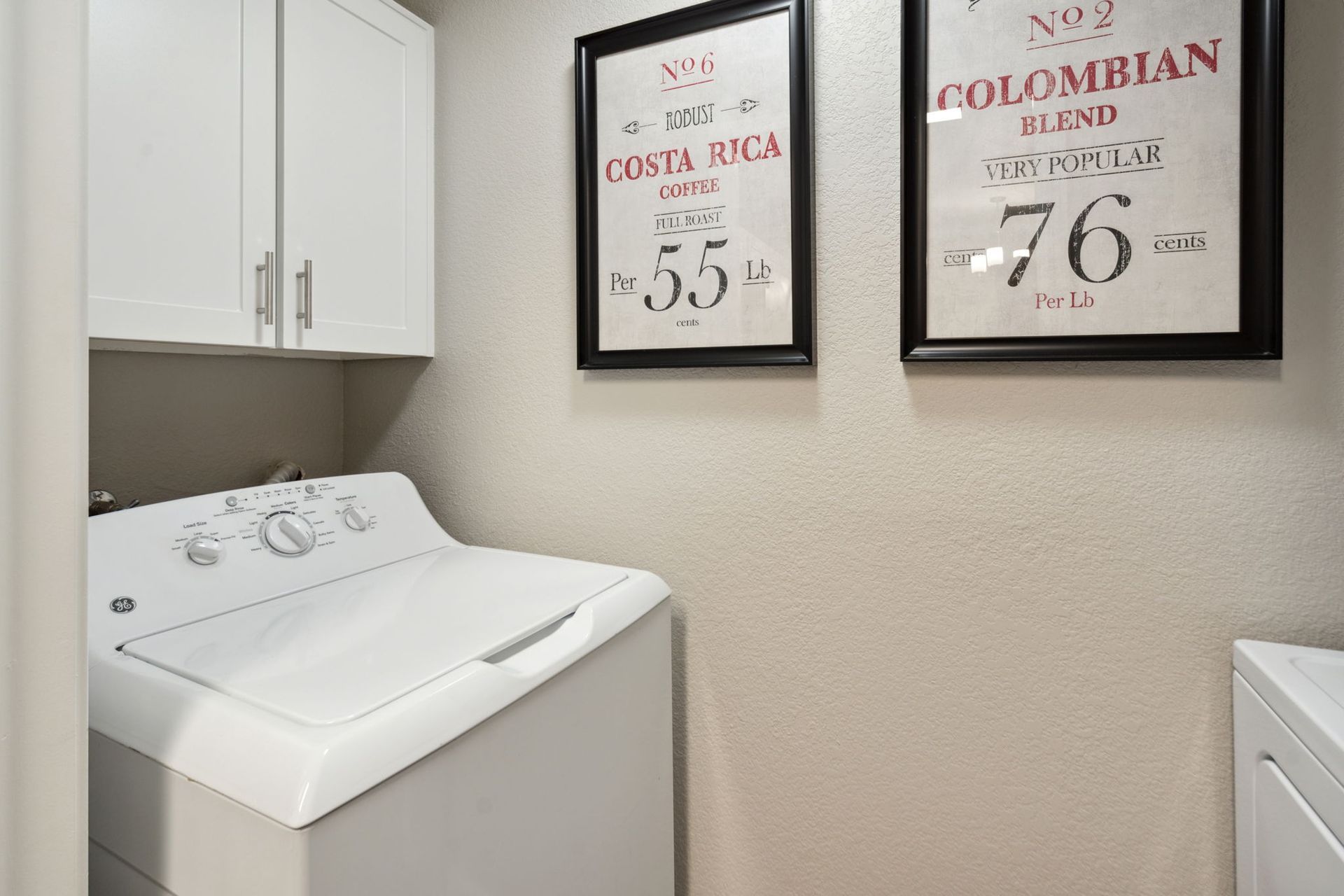 Laundry room with white washer and dryer, cabinets, and framed artwork at River Oaks.