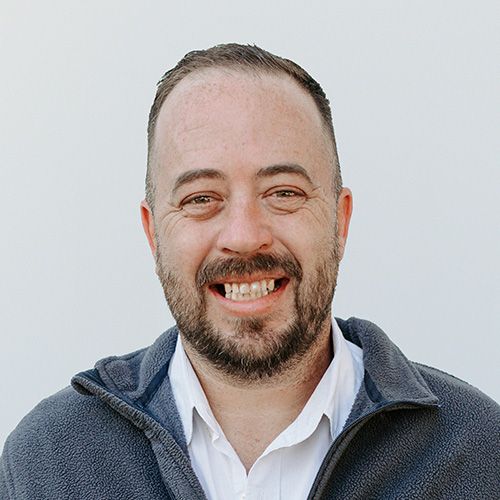 A man with a beard is smiling and wearing a gray jacket.