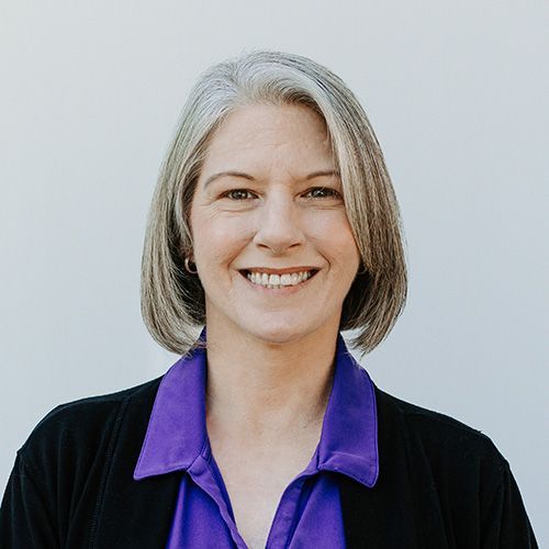 A woman wearing a purple shirt and a black jacket is smiling for the camera.