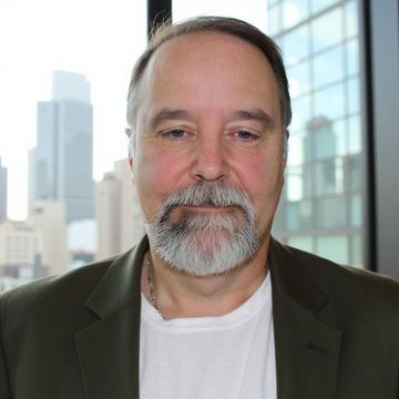 Portrait of a man in a dark blazer and white shirt with city buildings in the background