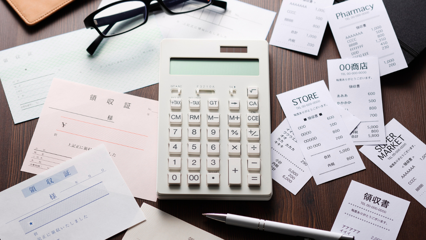 Calculator on a desk surrounded by receipts, bills, and glasses, suggesting budgeting or tax work