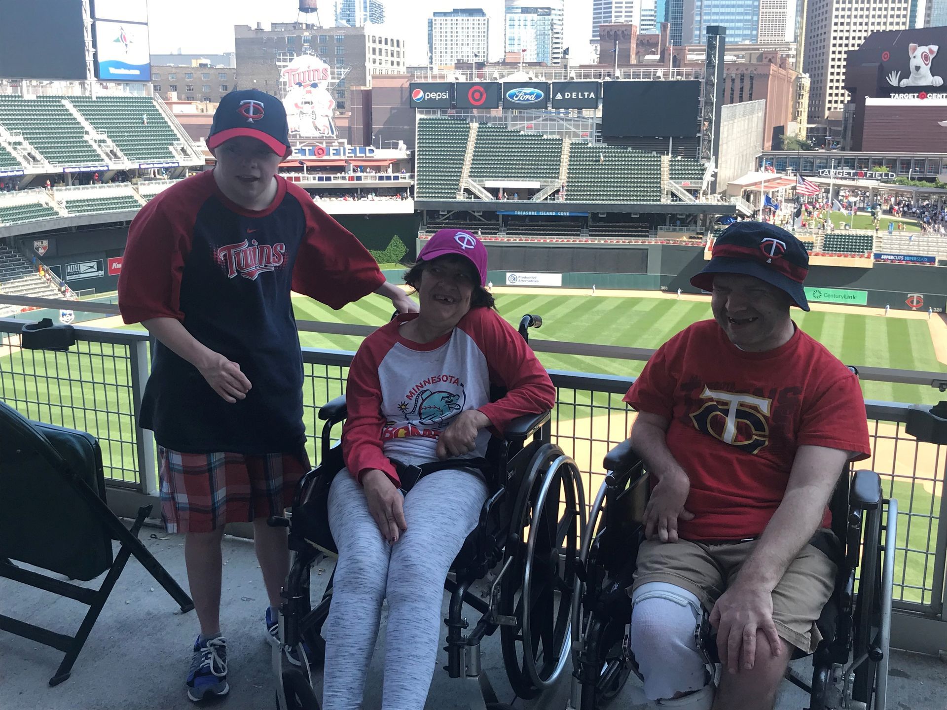 Three people in wheelchairs are standing in front of a baseball field.