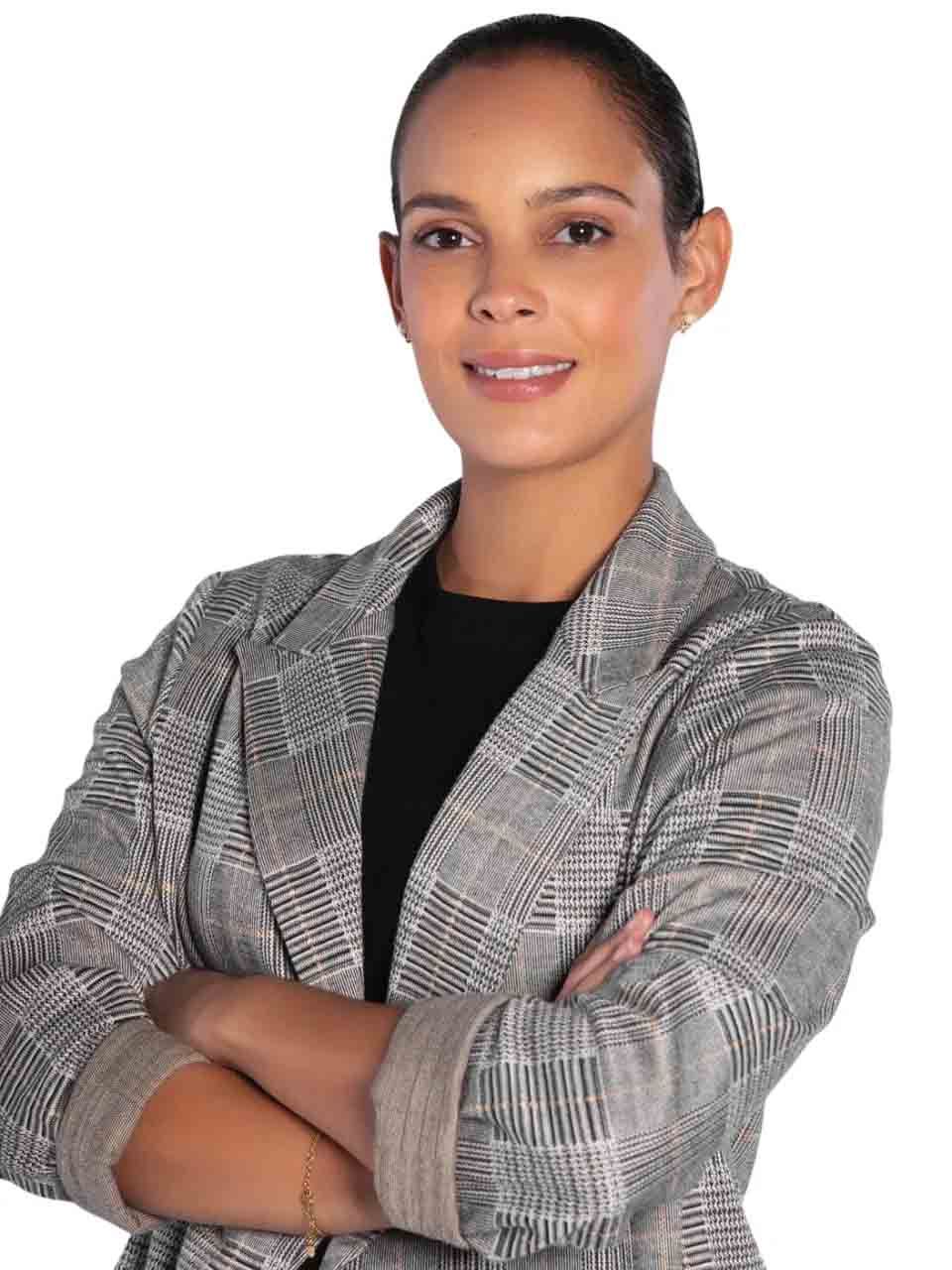 Personne les bras croisés, portant un blazer gris à carreaux et un haut noir, souriant sur fond blanc
