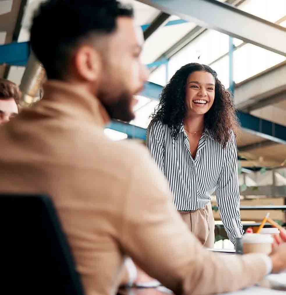 Colleagues collaborating in a bright office, with one woman smiling and leaning over a table.