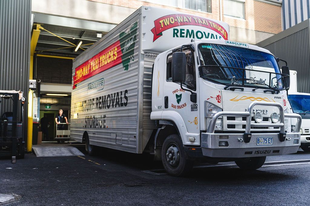 White moving truck at a loading dock with large red and yellow signage, parked outside a warehouse