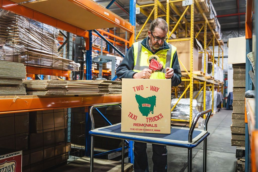 Man in warehouse holding protest sign that reads “We are tired” beside shelves and pallets