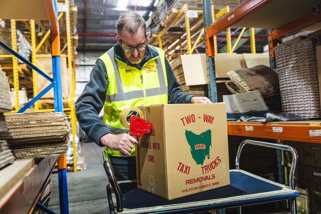 Worker in a warehouse packing a gift box labeled “Merry Christmas” on a cart