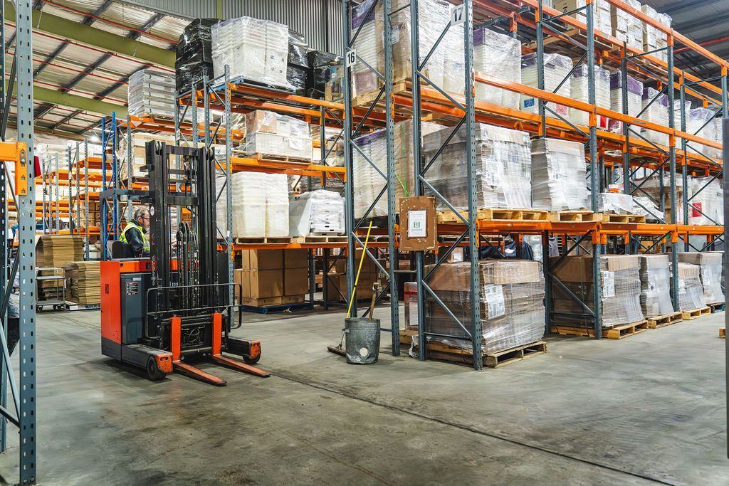A man is kneeling down in a warehouse looking at boxes.