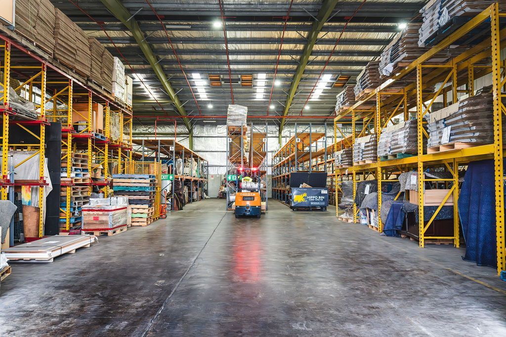 Warehouse aisle with forklifts, tall yellow racks, and stacked goods under bright industrial lights