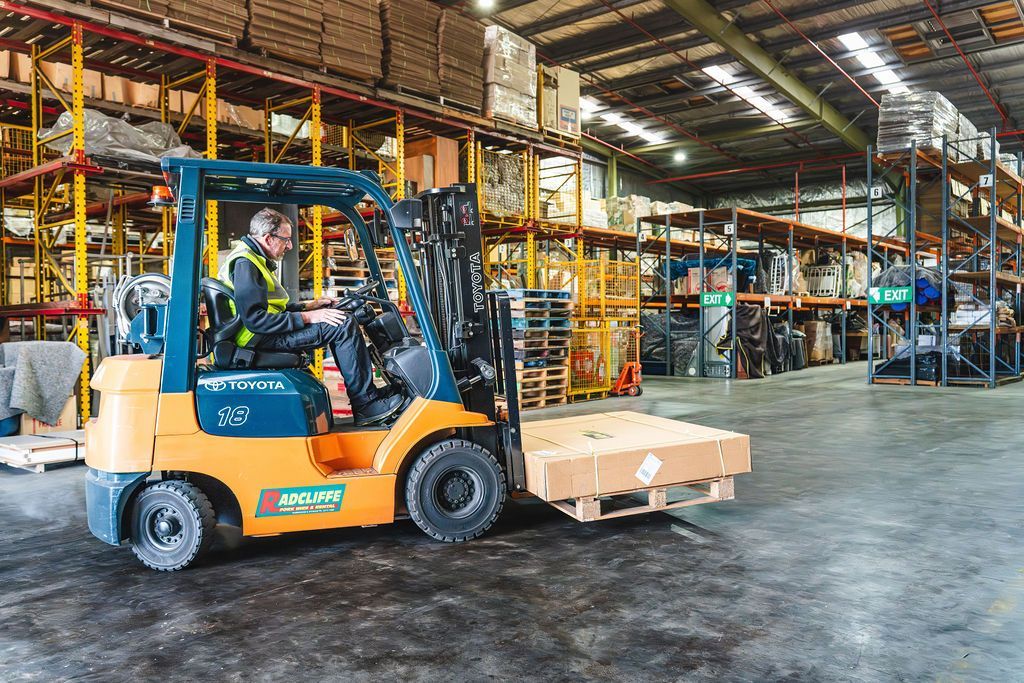 Orange forklift in a warehouse moving stacked boxes across a concrete floor