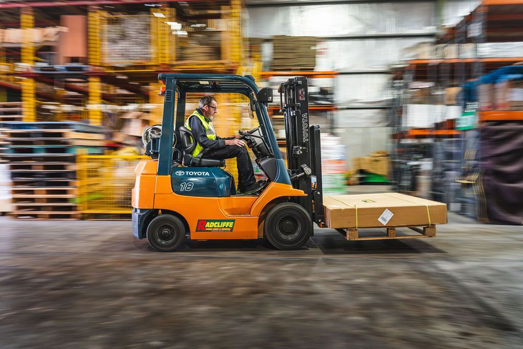 Orange forklift carrying boxes in a warehouse aisle with motion blur