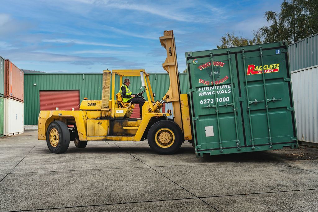 Yellow forklift pushing a green shipping container in an industrial yard