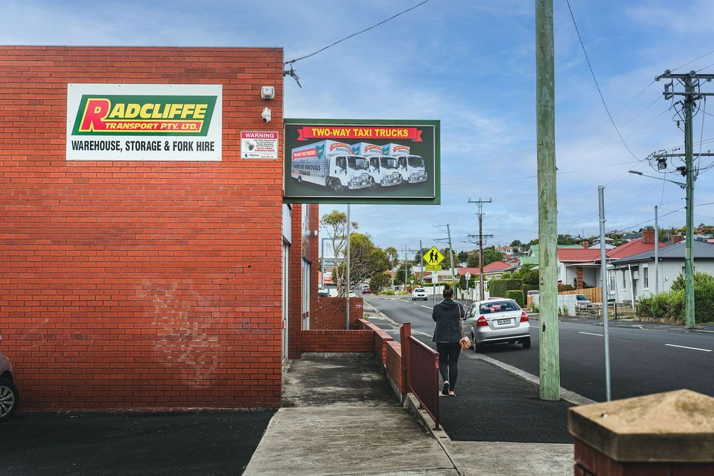 Street scene with brick building, billboards, sidewalk, parked cars, and a pedestrian on a wet road