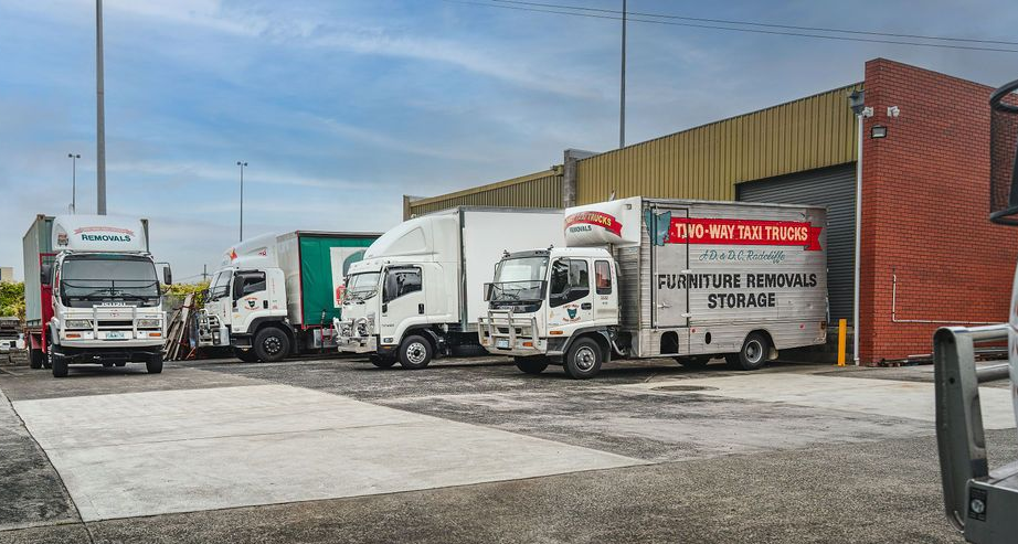 Semi-trucks parked outside a brick warehouse under a cloudy sky