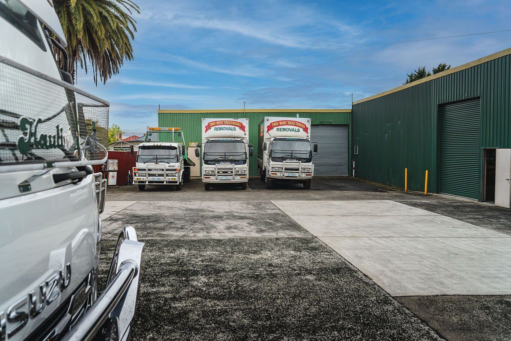 Parking lot with several white trucks in front of green garage doors on a sunny day.