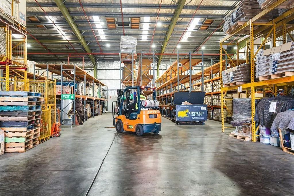 A forklift truck navigating through a warehouse filled with tall shelves stacked with various items.