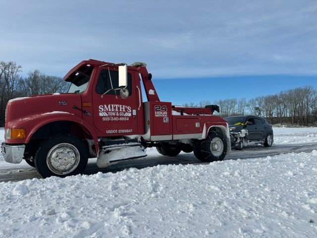 Red tow truck on snowy roadside towing a dark SUV under a cloudy sky