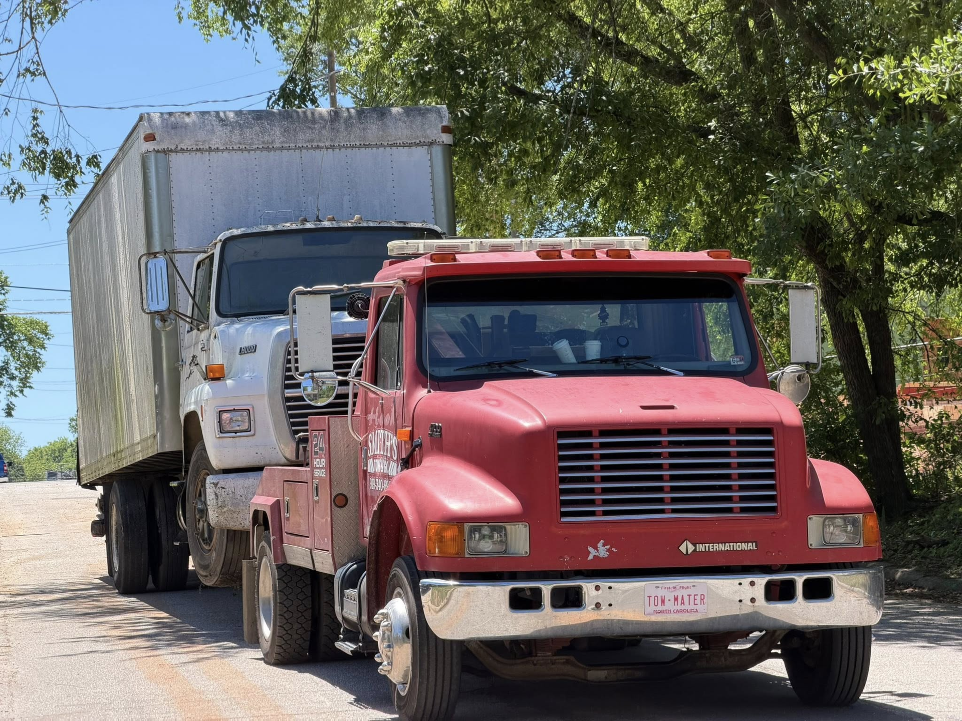 Red truck towing a white semi-trailer on a tree-lined road