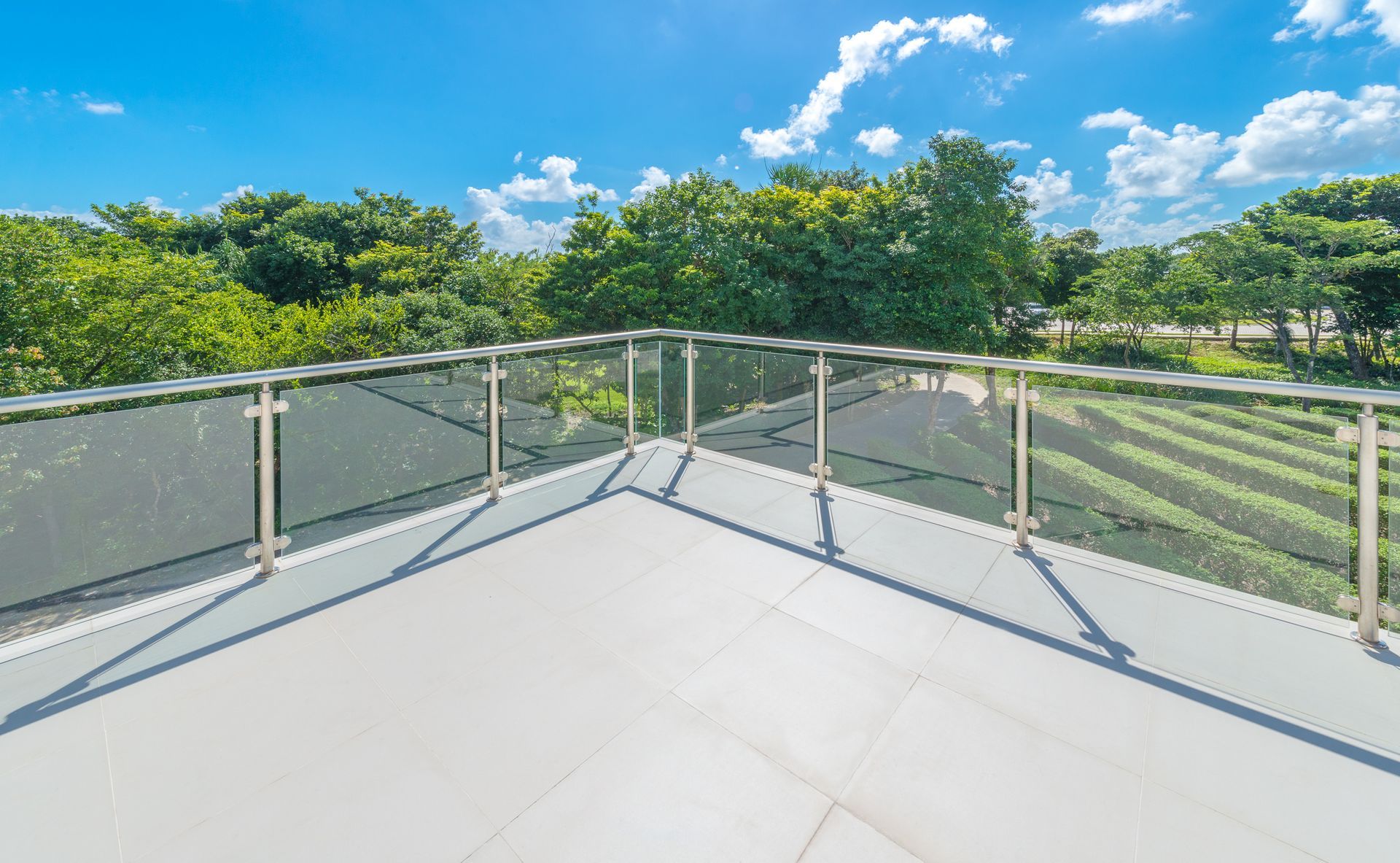 Sunny rooftop terrace with glass railing overlooking green trees and blue sky